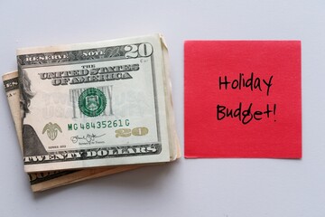 Cash Dollars money and red note with text written HOLIDAY BUDGET, concept of set budget for holiday celebration expenses, financial planning on christmas new year holiday spending