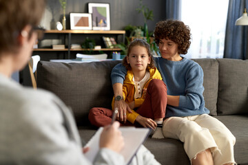 Mother sitting on sofa together with her son in living room and talking to child psychologist