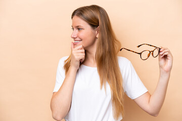 Young pretty blonde woman with glasses isolated on beige background thinking an idea and looking side