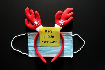 Red reindeer headband , face mask and a yellow sticky note written HAVE A  SAFE CHRISTMAS, concept...