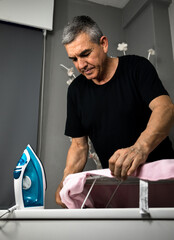 60-year-old man doing housework, ironing clothes.