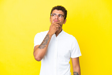 Young handsome Brazilian man isolated on yellow background having doubts