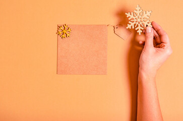 A woman's hand holds a wooden snowflake and a craft card next to it on a beige background.