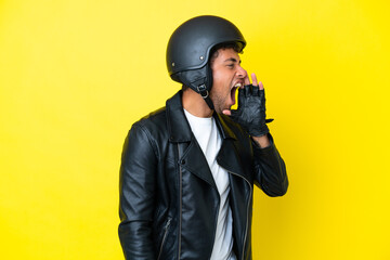 Young Brazilian man with a motorcycle helmet isolated on yellow background shouting with mouth wide...