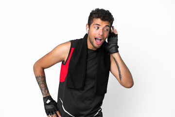 Sport brazilian man with towel isolated on white background listening to something by putting hand on the ear