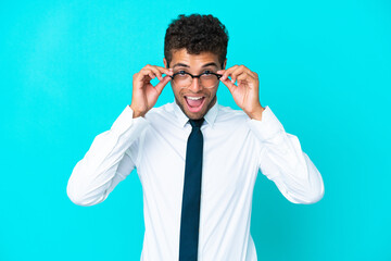 Young business Brazilian man isolated on blue background with glasses and surprised