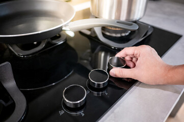 Male hand turning switch knob on modern gas stove in kitchen showroom. Cooking appliance in domestic kitchen. Home improvement and House interior design concepts