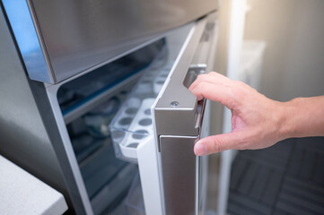Male hand opening fridge or refrigerator door in kitchen showroom. Buying appliance for home interior design.