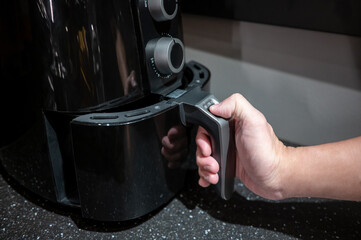 Male hand holding an electric air fryer handle in the kitchen. Home appliance for healthy cooking lifestyle. - 547662570