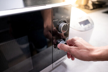 Male hand turning temperature knob of modern microwave in kitchen showroom. Buying cooking...