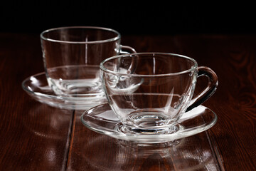 Two clean empty glass tea cups with saucers on a wooden table background. Selective focus.