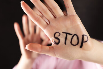 Woman with word Stop written on hand against dark background, closeup. Domestic violence concept - obrazy, fototapety, plakaty