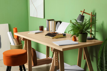Writer's workplace with typewriter on wooden desk near pale green wall in room
