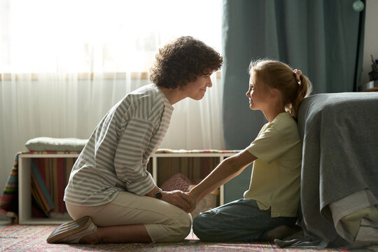 Young Mother Playing With Her Little Daughter During Her Leisure Time, They Sitting On Floor In Bedroom And Smiling To Each Other