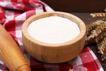 Flour in bowl and ears of wheat on wooden table, closeup