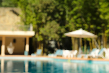 Blurred view of clear pool, sunbeds and umbrella outdoors