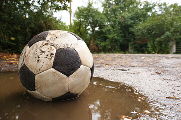 Fototapeta na wymiar Dirty soccer ball in muddy puddle, space for text