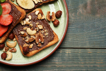 Tasty toasts with chocolate spread, nuts, strawberries and banana served on wooden table, top view. Space for text