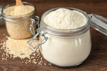Jars with quinoa flour and seeds on wooden table, closeup
