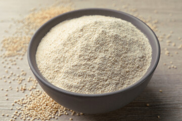 Ceramic bowl with quinoa flour and seeds on wooden table, closeup