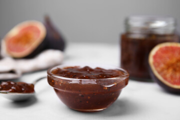 Tasty sweet fig jam and fruits on white marble table, closeup