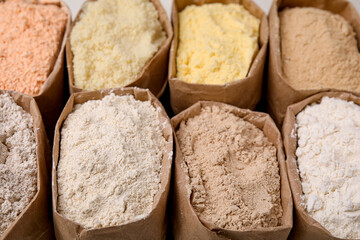 Fototapeta na wymiar Paper sacks with different types of flour as background, closeup