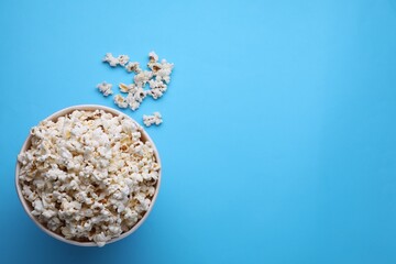 Paper bucket with delicious popcorn on light blue background, flat lay. Space for text