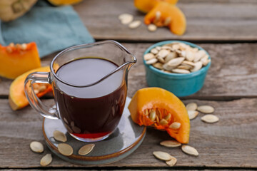 Fresh pumpkin seed oil in glass pitcher on wooden table. Space for text