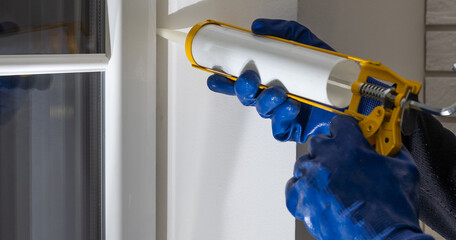 Construction worker sealing window with caulk indoors