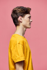 a man in a yellow tank top poses sideways to the camera on a pink background