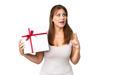 Middle age caucasian woman holding a gift over isolated background intending to realizes the solution while lifting a finger up