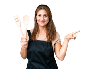 Middle age caucasian woman holding a rolling pin over isolated background pointing finger to the side