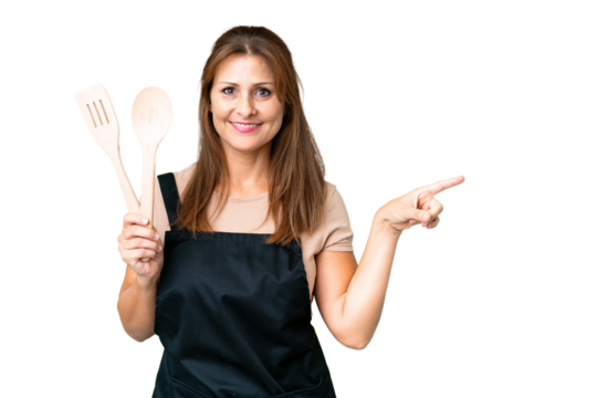 Middle age caucasian woman holding a rolling pin over isolated background pointing finger to the side