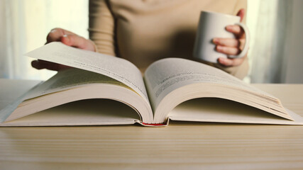 Woman is sitting and reading a book for study to prepare for examination or relax on leisure day with drink coffee.