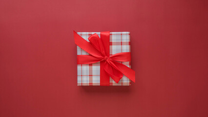 Square gift box with a red bow on a red background top view