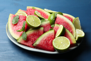 Plate with cut juicy watermelon and lime on blue wooden table