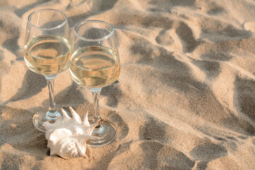 Glasses of tasty wine and seashell on sand, space for text