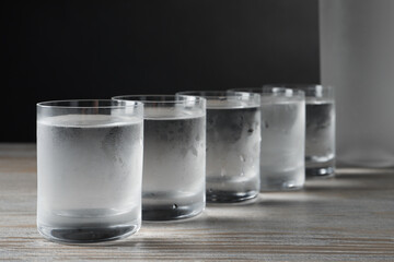 Shot glasses of cold vodka on wooden table against grey background, closeup