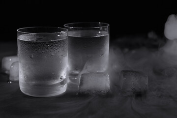Vodka in shot glasses with ice on table against black background, closeup
