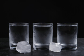 Vodka in shot glasses with ice on table against black background