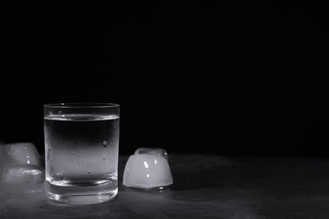 Vodka in shot glass with ice on table against black background