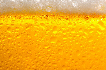 Glass of tasty cold beer with foam and condensation drops as background, closeup