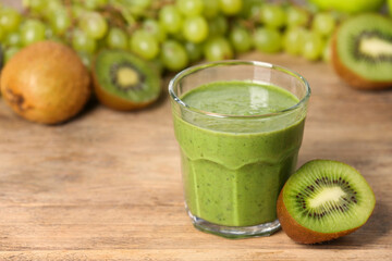 Glass of fresh green smoothie and ingredients on wooden table, space for text