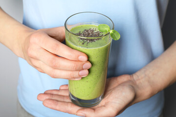 Woman holding glass of fresh green smoothie with chia seeds on grey background, closeup
