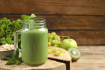 Mason jar of fresh green smoothie and ingredients on wooden table, space for text