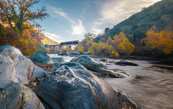 A train crosses the Pont d'Albano bridge over the Golo river lined by autumnal trees and boulders at Torrent de Cipetto near Barchcetta in Corsica