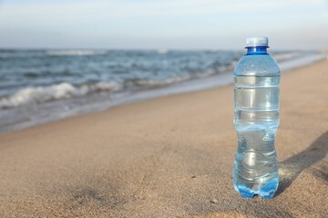 Plastic bottle of fresh water on wet sand near sea. Space for text