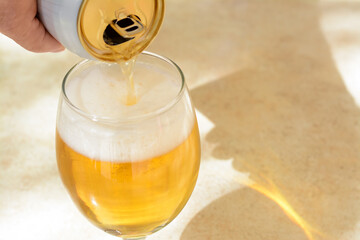 Man pouring beer from can into glass at table, closeup. Space for text