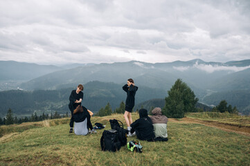 Fototapeta premium A group of young people tourists sit in the mountains on the ground in the mountains and rest during the hike against the background of beautiful views of the Carpathians.