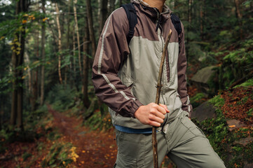 A male tourist in casual clothes walks with a stick in his hand along a forest path climbing the mountains with a serious face. Tourism concept.